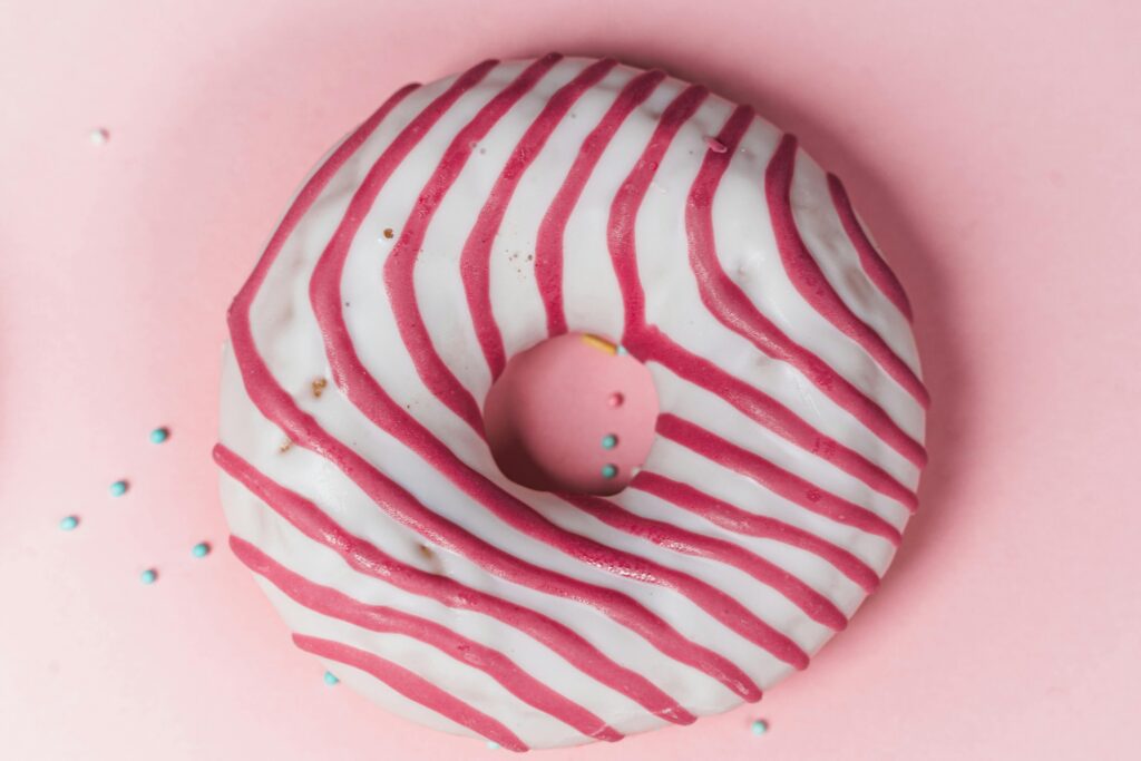 Delicious striped glazed donut on a pastel pink background, perfect for dessert lovers.