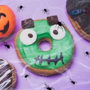 Halloween-themed donuts with scary designs and spider decorations on a purple background.